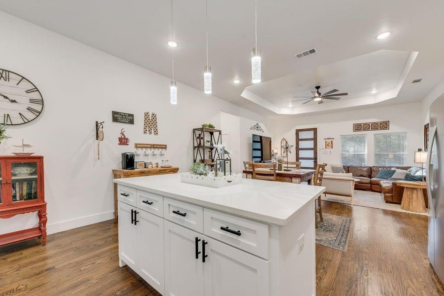 Kitchen with open floor plan, dark wood-style flooring, white cabinets, a center island, and a raised ceiling