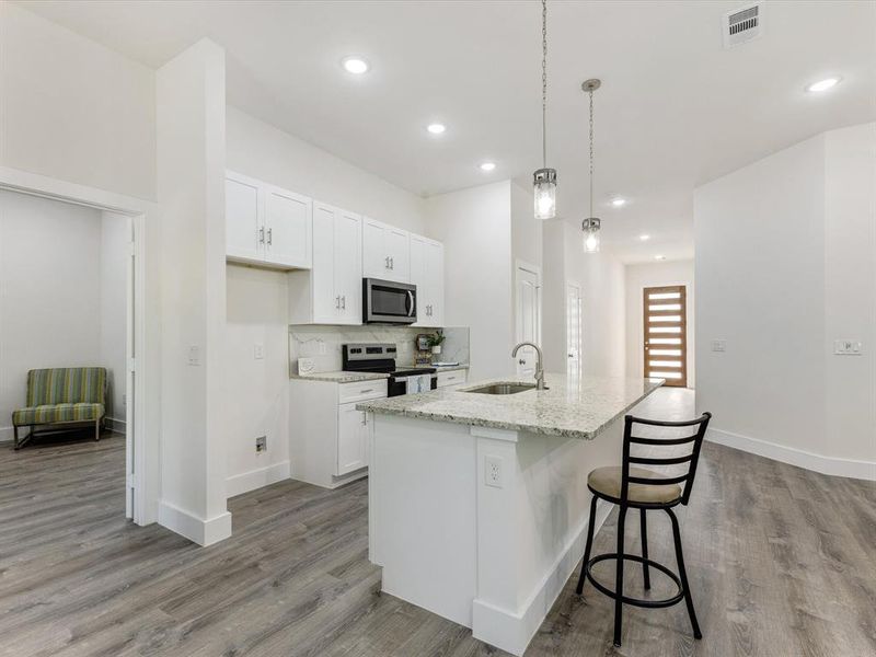 Kitchen with white cabinets, a breakfast bar, stainless steel appliances, light stone counters, and decorative light fixtures