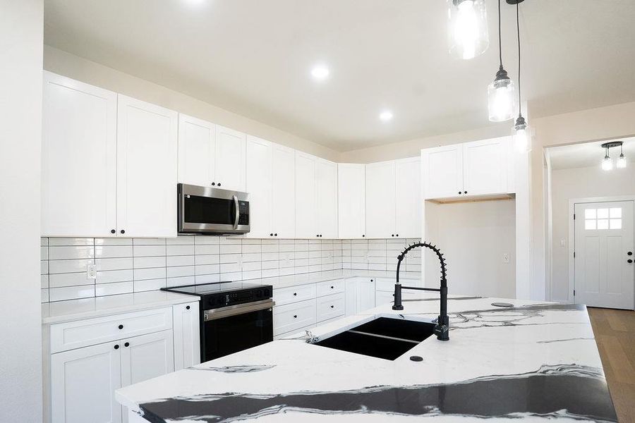 Kitchen with hanging light fixtures, electric range, stainless steel microwave, a center island with sink, and white cabinets
