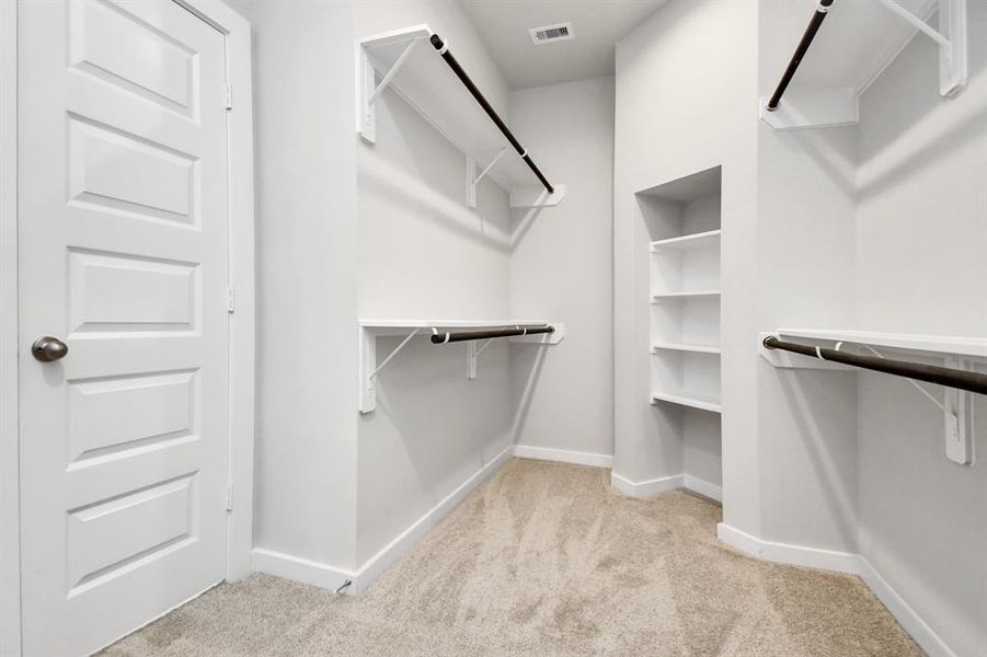 Experience luxury in this spacious walk-in closet with high ceilings and plush carpet. Warm paint tones, built-in shelving, and dark finishes create a contemporary and functional retreat. Sample photo, as built color and selections will vary.