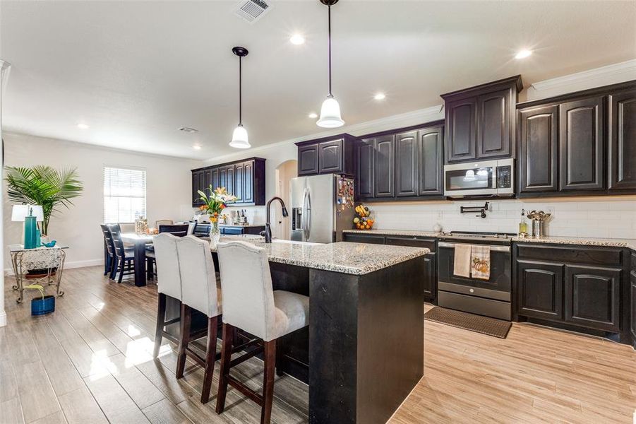 Kitchen with a kitchen breakfast bar, tasteful backsplash, stainless steel appliances, light wood-type flooring, and a kitchen island with sink