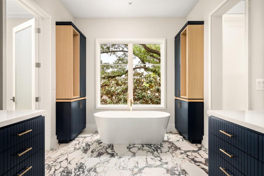 A spa-like moment unfolds with a freestanding soaking tub positioned beneath a window of greenery and framed by architectural symmetry.