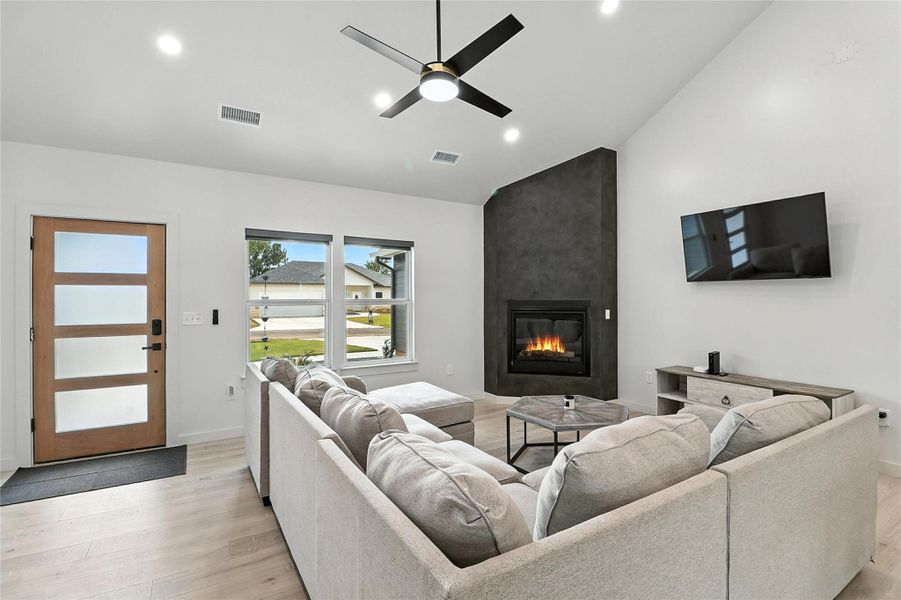 Living area with a large fireplace, light wood finished floors, recessed lighting, ceiling fan, and high vaulted ceiling