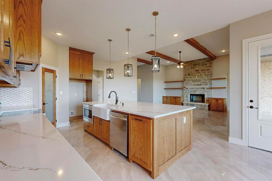 Kitchen featuring light stone counters, an island with sink, beamed ceiling, appliances with stainless steel finishes, and a fireplace