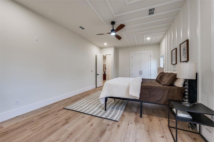 Spacious room featuring wood-finish flooring, a decorative tray ceiling with a ceiling fan, and white walls