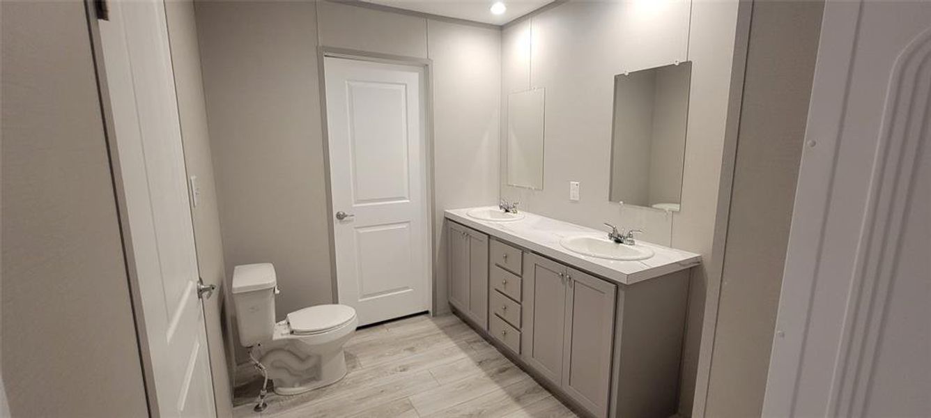 Bathroom featuring double vanity, toilet, wood finished floors, and a sink