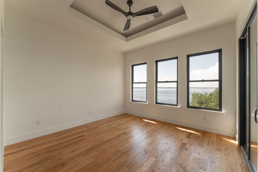 Spare room featuring a tray ceiling, light wood finished floors, a ceiling fan, and a water view