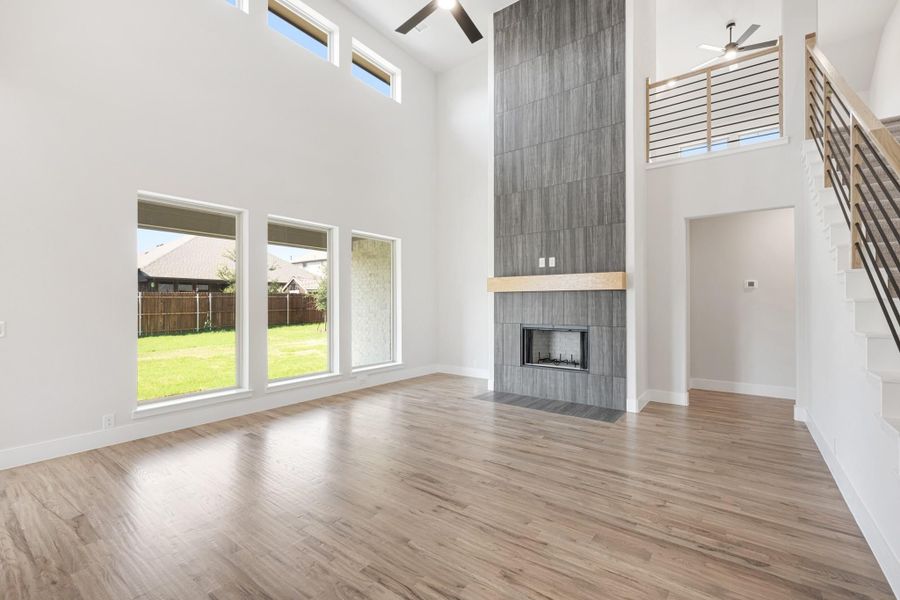 Open living room with two-story ceiling, floor-to-ceiling tiled fireplace, and wood floors