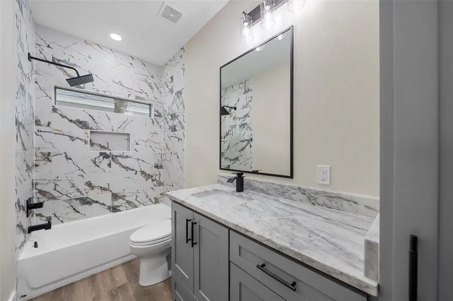Bathroom with wood finished floors, toilet, vanity, shower / tub combination, and recessed lighting