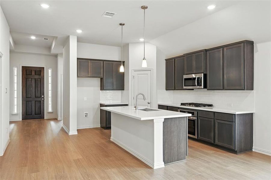 Kitchen with decorative backsplash, pendant lighting, stainless steel appliances, dark brown cabinetry, and light wood finished floors Kitchen with decorative backsplash, pendant lighting, stainless steel appliances, dark brown cabinetry, and light wood finished floors