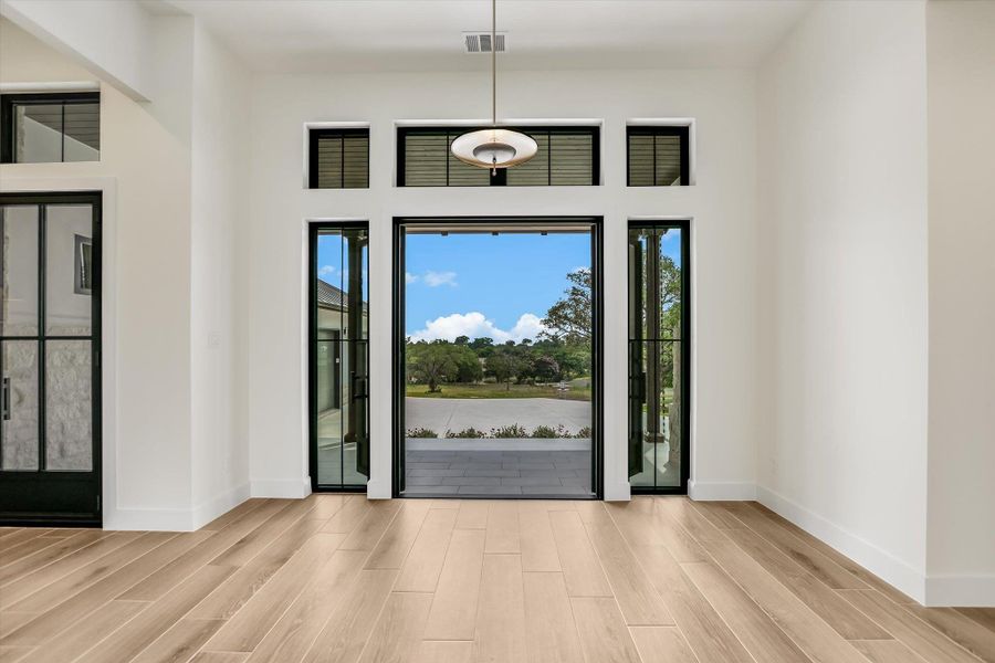 Grand entryway featuring light wood-finish flooring, a contemporary pendant light fixture, and floor-to-ceiling glass doors with transom windows