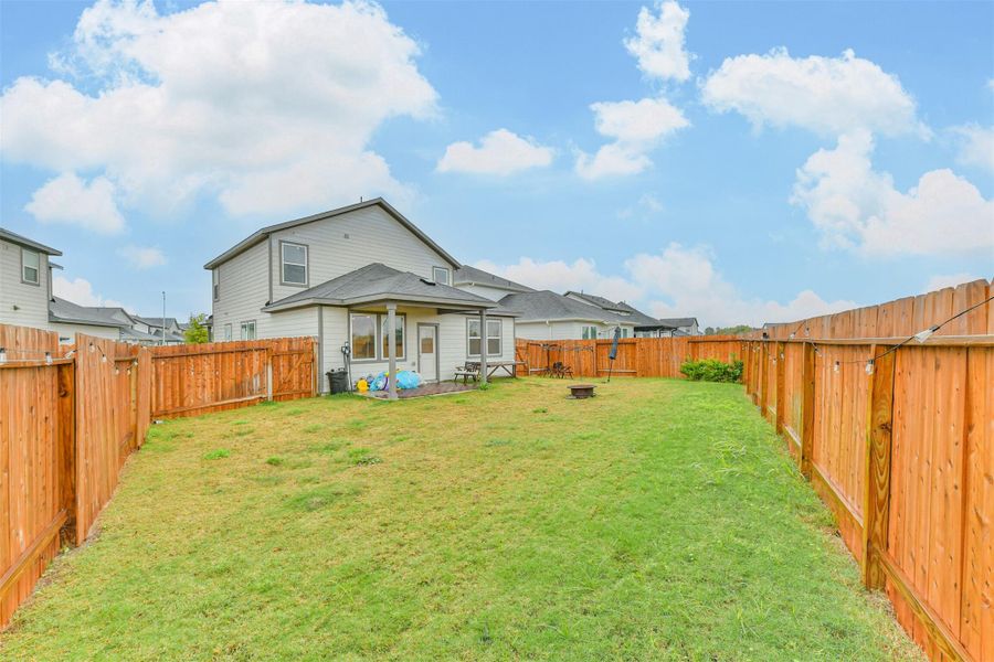 Spacious backyard with a well-maintained lawn, enclosed by a wooden fence. Features a covered patio area ideal for outdoor activities and relaxation.