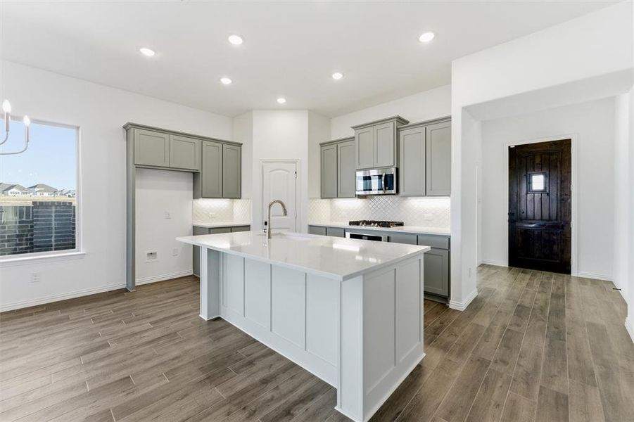 Kitchen with a center island with sink, light stone countertops, light wood-style floors, stainless steel microwave, and recessed lighting