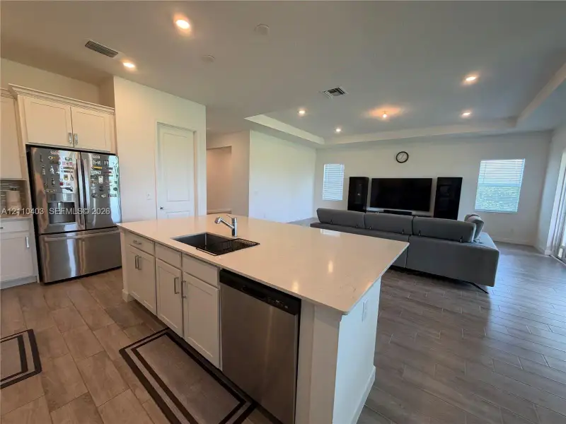 Kitchen featuring a central island with a quartz countertop, stainless steel appliances, white cabinetry, recessed lighting, and wood-finish flooring