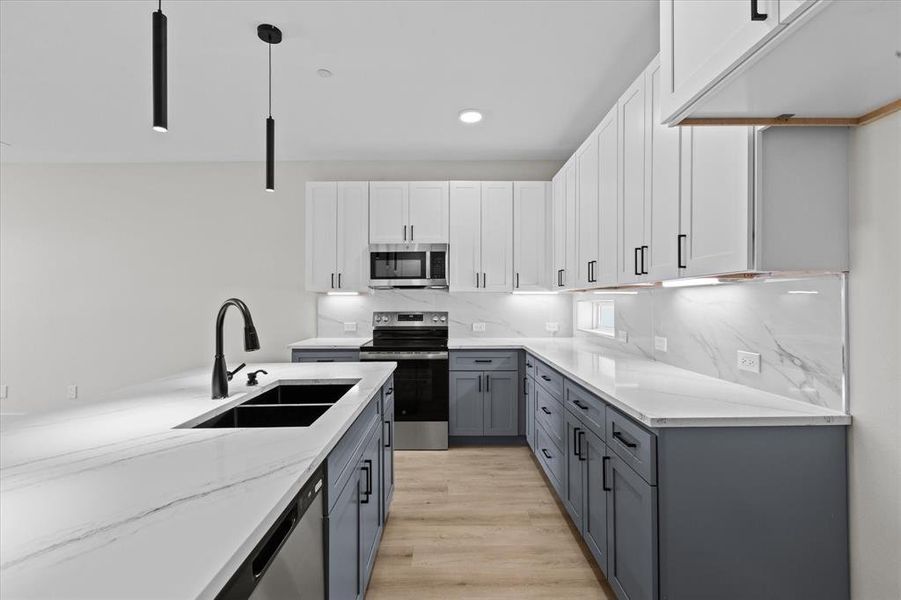 Kitchen featuring gray cabinetry, appliances with stainless steel finishes, light stone countertops, light wood-style flooring, and hanging light fixtures