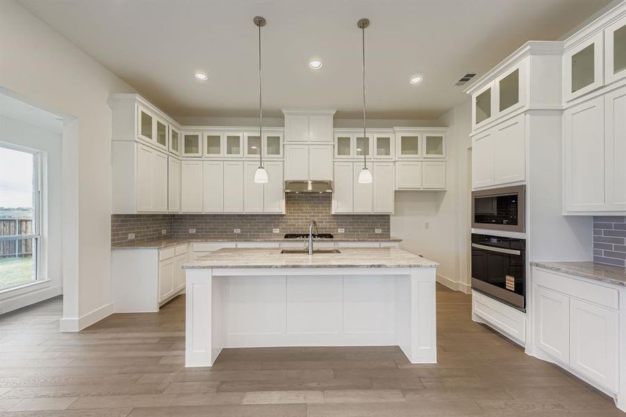 Kitchen featuring decorative backsplash, stainless steel appliances, white cabinets, light stone counters, and pendant lighting Kitchen featuring decorative backsplash, stainless steel appliances, white cabinets, light stone counters, and pendant lighting