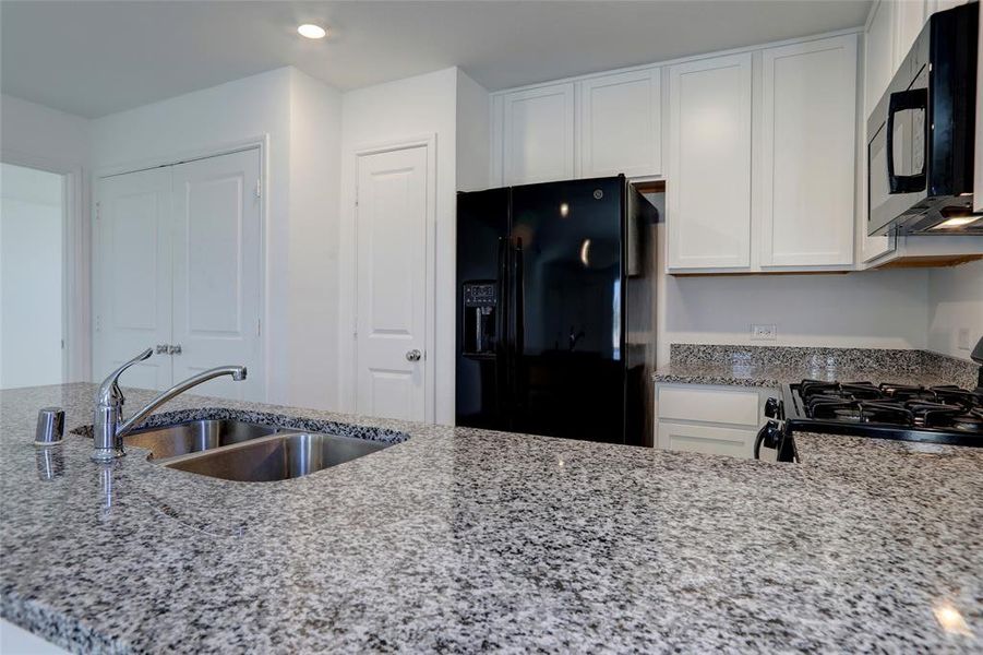 Kitchen with light stone countertops, black appliances, white cabinetry, and recessed lighting