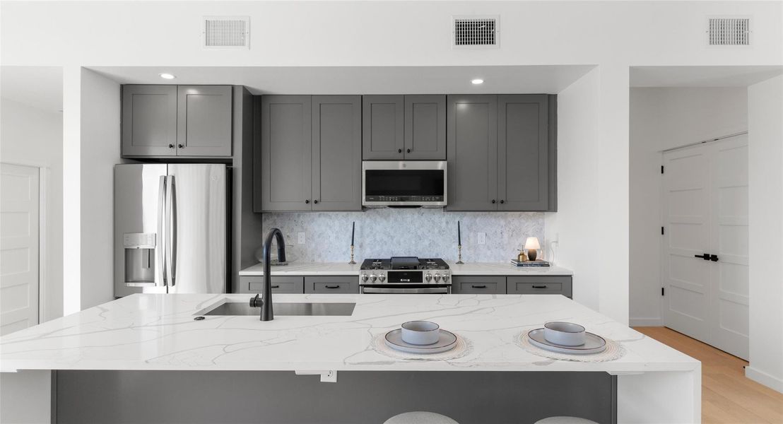 The island kitchen pairs stainless appliances with room to gather — ideal for cooking together or hosting friends. Model No. 105 Shown.