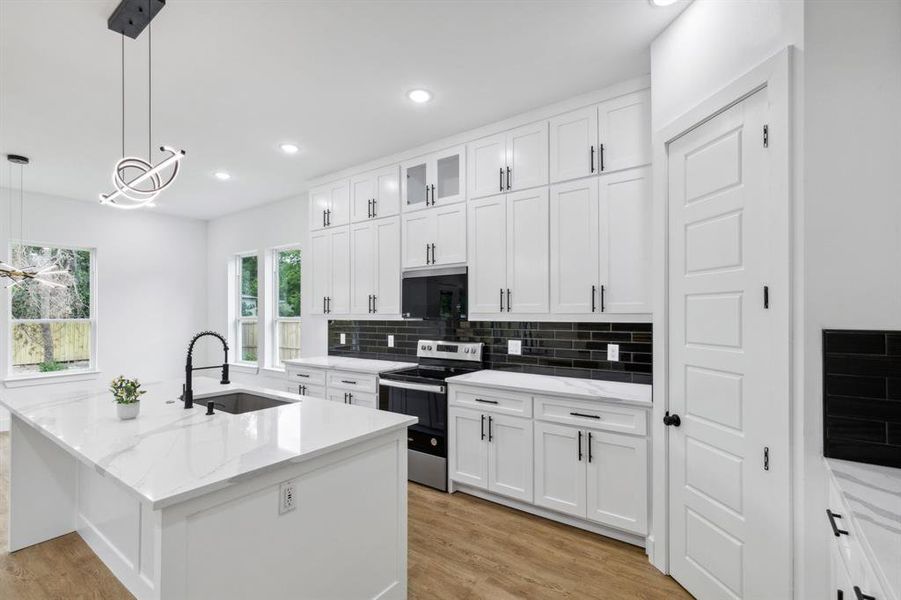 Kitchen with light hardwood / wood-style floors, white cabinetry, electric stove, and an island with sink