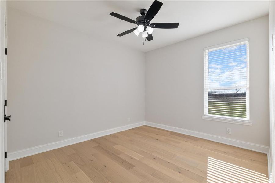 Spare room featuring light wood-style floors, plenty of natural light, baseboards, and a ceiling fan