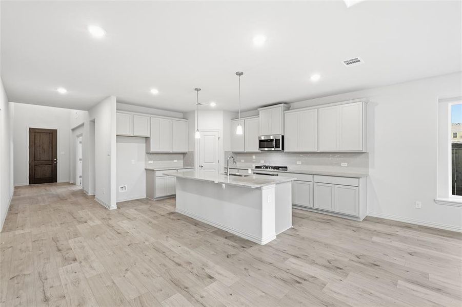 Kitchen featuring a kitchen island with sink, decorative light fixtures, light wood-style floors, white cabinetry, and stainless steel appliances