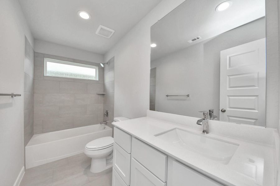 Secondary bath features tile flooring, bath/shower combo with tile surround, light stained wood cabinets, beautiful light countertop. Sample photo of completed home with similar floor plan. Actual colors and selections may vary.