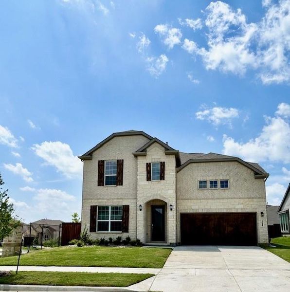 Two-story residence featuring a stone and stucco exterior, arched entry, dark wood-finish garage door, exterior lighting fixtures, and a concrete driveway