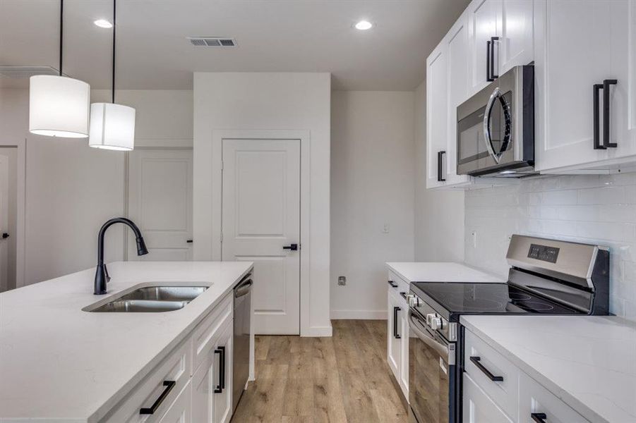 Kitchen with appliances with stainless steel finishes, white cabinets, pendant lighting, light stone countertops, and light wood-style floors Kitchen with appliances with stainless steel finishes, white cabinets, pendant lighting, light stone countertops, and light wood-style floors