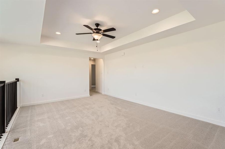 Unfurnished room featuring a tray ceiling, ceiling fan, and light colored carpet