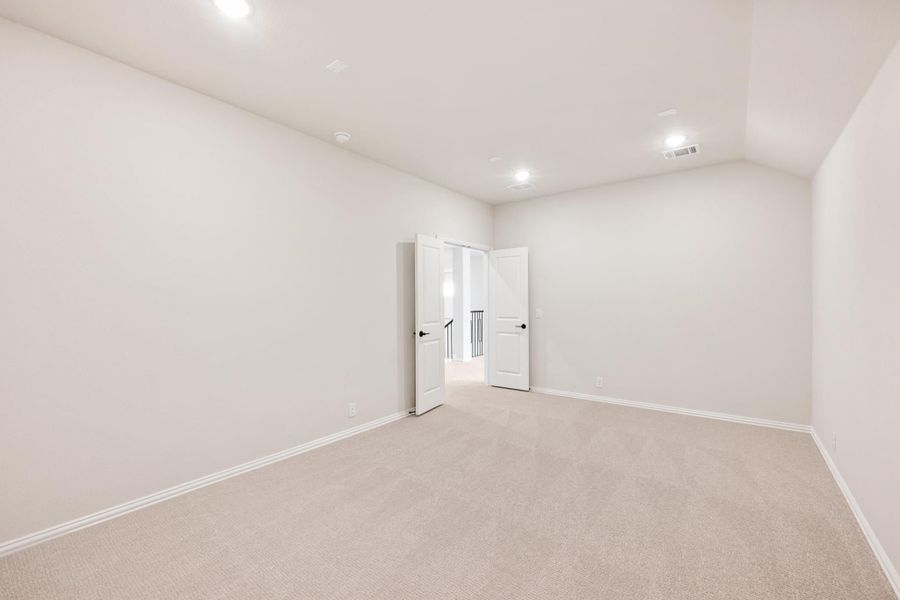 Empty bedroom with beige carpet, white walls, recessed lighting, and open double doors leading to hallway