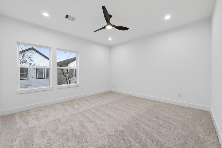 This room features a spacious layout with clean white walls. It has large windows for natural light and a modern ceiling fan with recessed lighting, creating a bright and airy atmosphere.