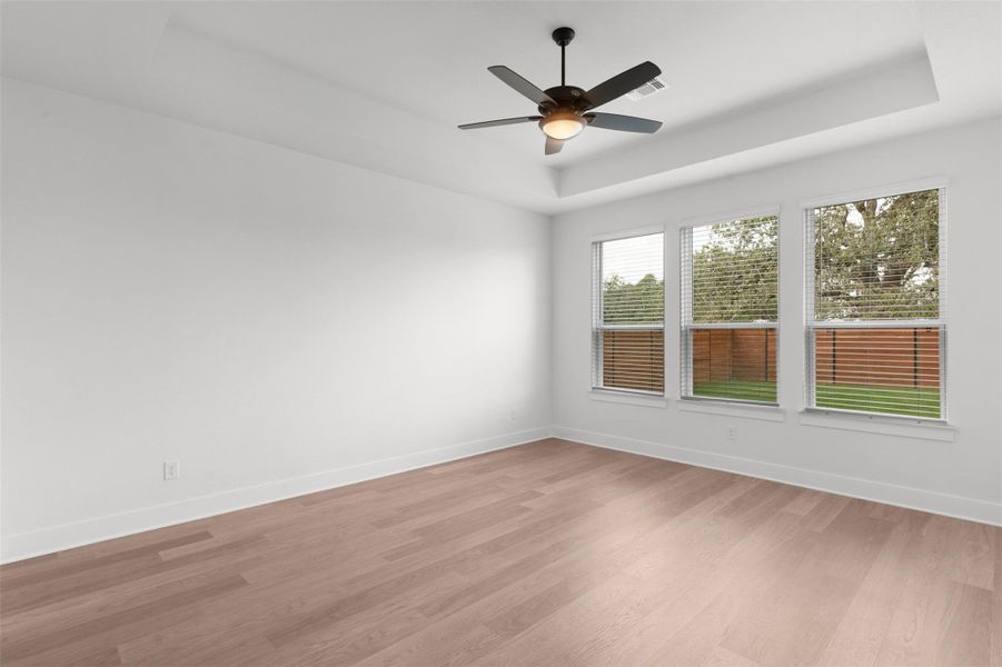 Unfurnished room featuring a tray ceiling, light wood-style floors, and ceiling fan