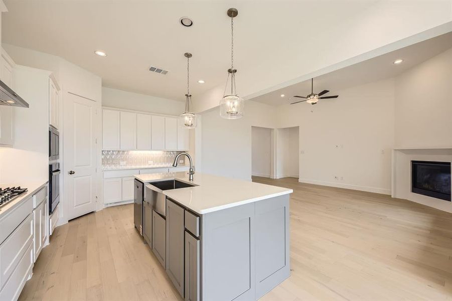 Dual tone kitchen featuring a center island with sink, open floor plan, tasteful backsplash, light wood-type flooring, and two tone color scheme