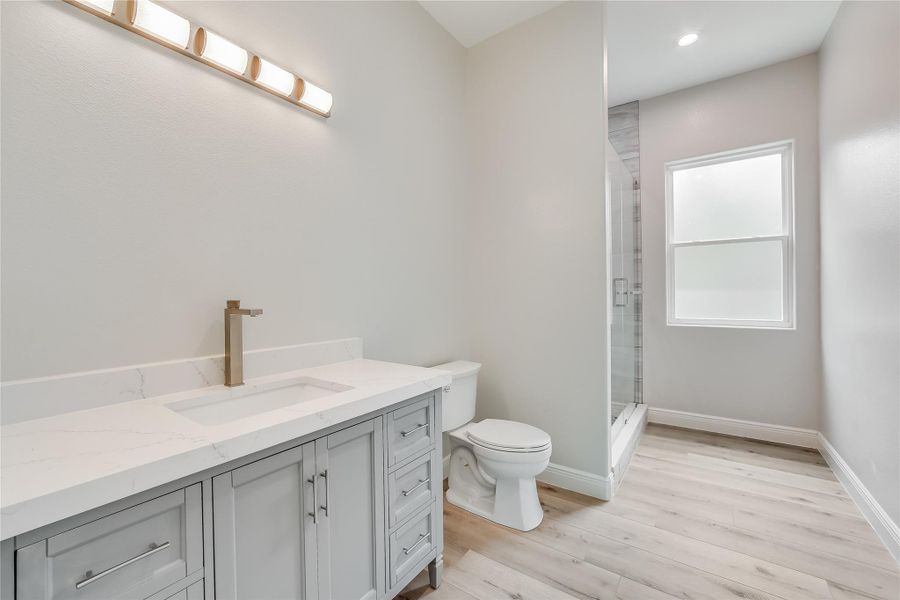 Bathroom with hardwood / wood-style floors, toilet, a shower with door, and vanity