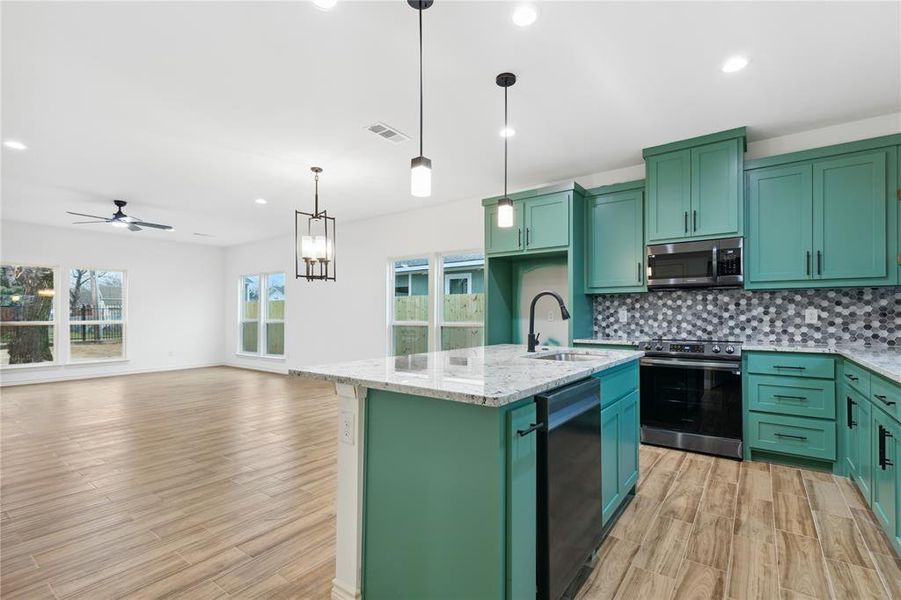 Kitchen with decorative light fixtures, ceiling fan with notable chandelier, stainless steel appliances, tasteful backsplash, and a kitchen island with sink