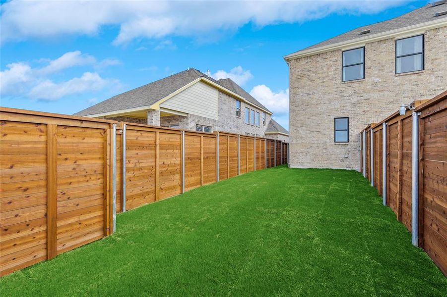 Expansive backyard featuring artificial turf, new wooden privacy fencing, and a brick exterior