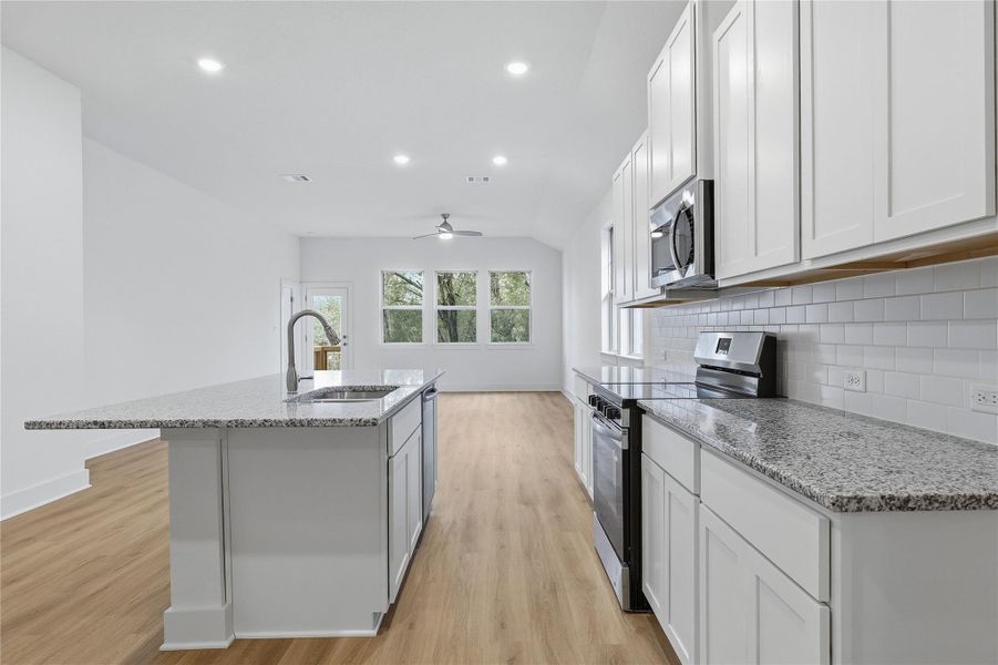 Kitchen with appliances with stainless steel finishes, light stone counters, an island with sink, backsplash, and white cabinetry