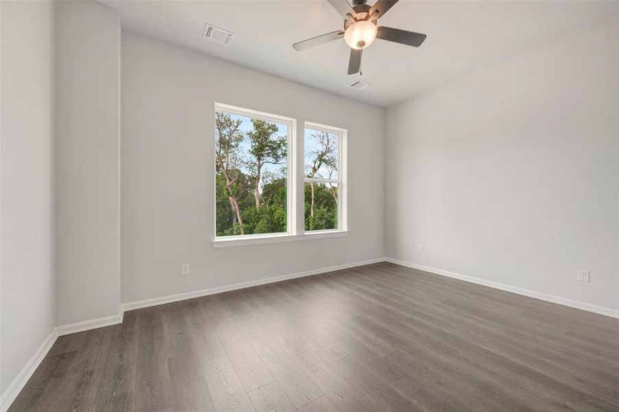 Spacious room featuring multiple windows, wood-finish flooring, a ceiling fan with light fixture, white walls, and white baseboards Spacious room featuring multiple windows, wood-finish flooring, a ceiling fan with light fixture, white walls, and white baseboards