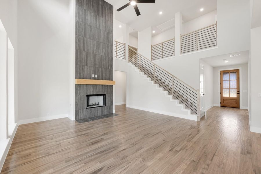 Open living room with two-story ceiling, tile fireplace, hardwood floors, and staircase with metal railing