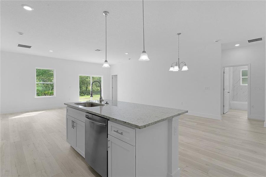 Kitchen island includes large single-bowl sink and dishwasher, and breakfast bar with pendant lights