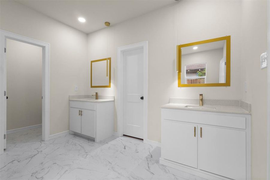 Bathroom featuring dual white vanities with light countertops, gold-framed mirrors, and brass-finish fixtures