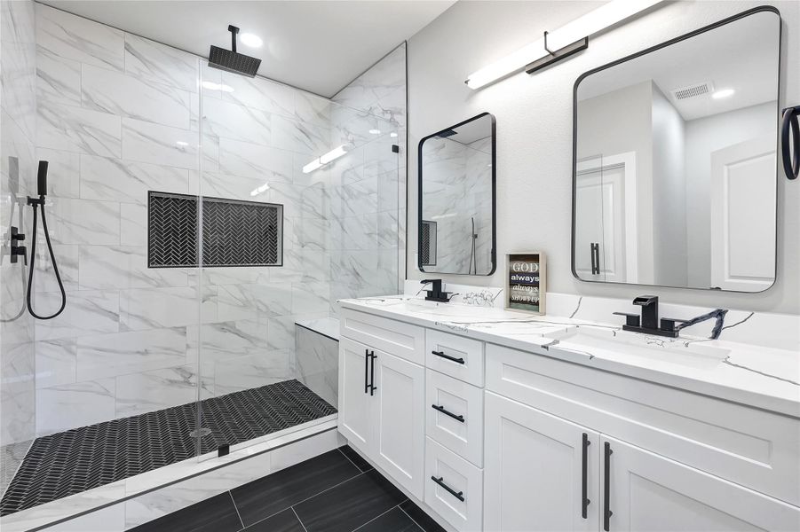 This modern bathroom features a spacious walk-in shower with elegant marble tile and a sleek black rain showerhead. The double vanity includes two large mirrors, black fixtures, and ample storage in white cabinetry, creating a sophisticated and functional space.