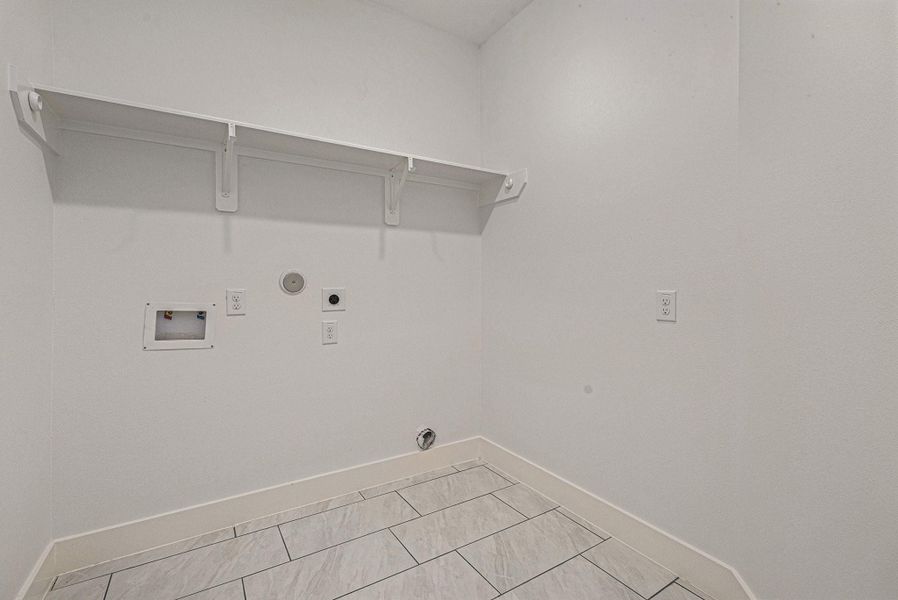 This is a utility room featuring tiled floors, hookups for a washer and dryer, and a shelf for storage.
