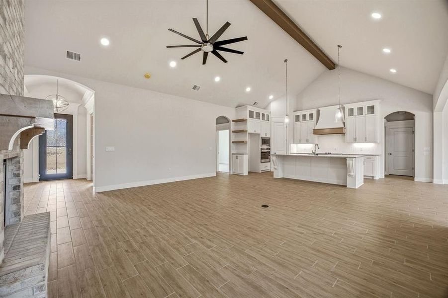 Unfurnished living room featuring arched walkways, a ceiling fan, wood tiled floors, recessed lighting, and a fireplace with raised hearth Unfurnished living room featuring arched walkways, a ceiling fan, wood tiled floors, recessed lighting, and a fireplace with raised hearth