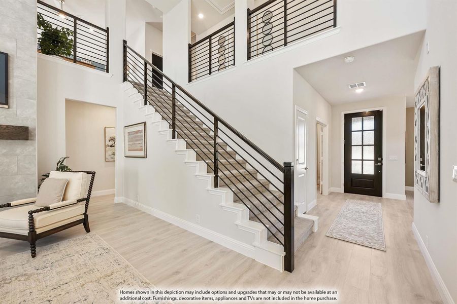 Two-story foyer with white staircase, black metal railing, hardwood floors, and glass-panel front door