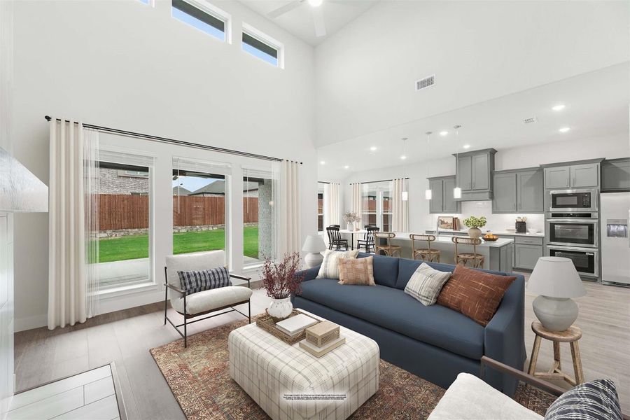Open-concept living room with two-story ceiling, blue sofa, and kitchen with gray cabinets visible in background