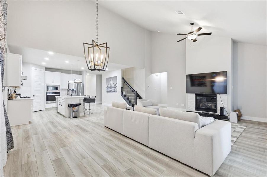 Living area with high vaulted ceiling, stairway, light wood-style floors, a ceiling fan, and a glass covered fireplace