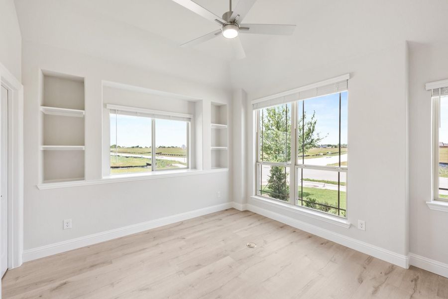 Empty bedroom with vaulted ceiling, ceiling fan, built-in shelves, and large windows with outdoor views