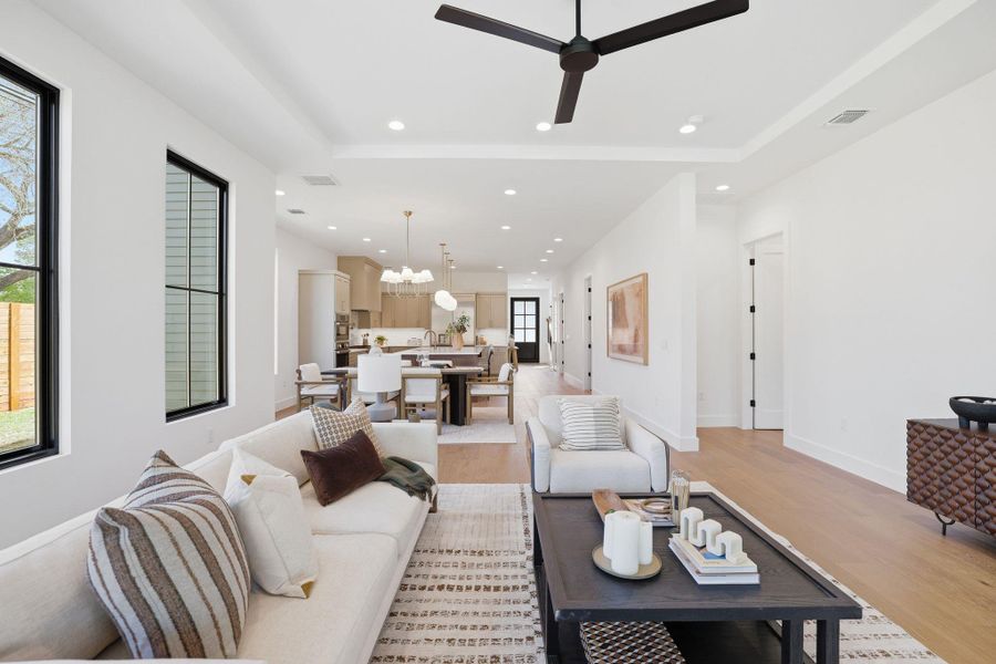 Living room featuring a tray ceiling, light wood-type flooring, a ceiling fan, and a chandelier