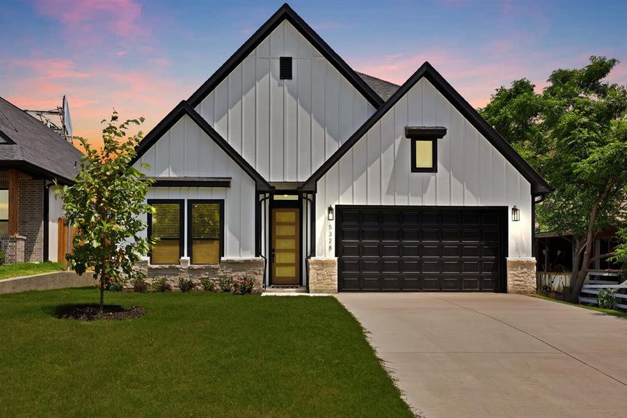 Modern farmhouse with board and batten siding, a front lawn, driveway, and stone siding Modern farmhouse with board and batten siding, a front lawn, driveway, and stone siding